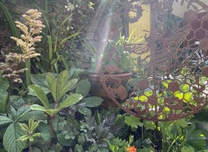 Decorative bee and honeycomb ironwork among lush planting in a small garden.
