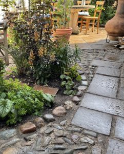 A path made of reclaimed cobbles and stone slabs winds through a small planted courtyard garden.