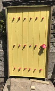 Salvaged door with red masking tape and painted yellow in a reclaimed courtyard garden in Cumbria