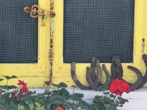 Found horseshoes and red geraniums at base of salvaged yellow window in a reclaimed courtyard garden